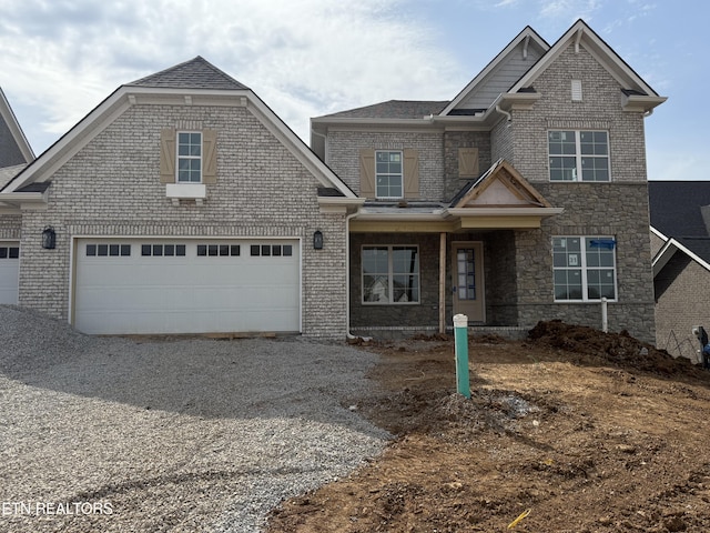 craftsman inspired home with gravel driveway, an attached garage, brick siding, and a shingled roof