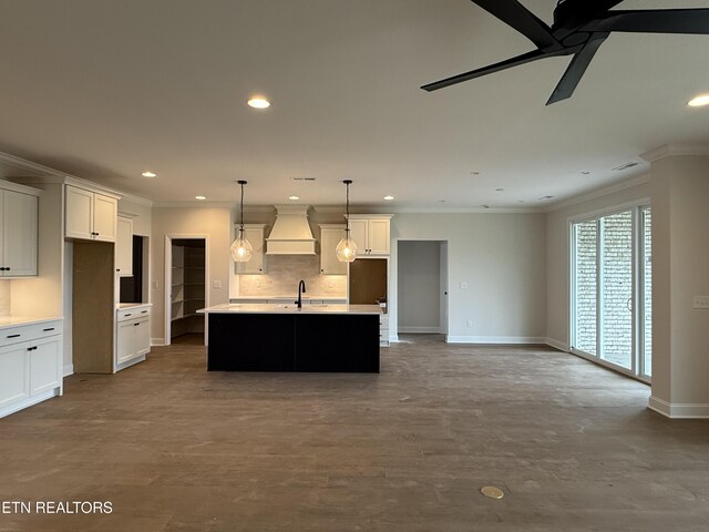 kitchen featuring a center island with sink, baseboards, custom exhaust hood, recessed lighting, and ornamental molding