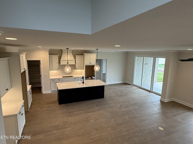 kitchen featuring dark wood finished floors, a center island with sink, baseboards, custom exhaust hood, and ornamental molding