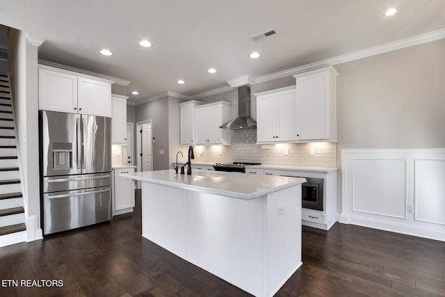 kitchen featuring visible vents, wall chimney range hood, light countertops, stainless steel fridge, and a sink