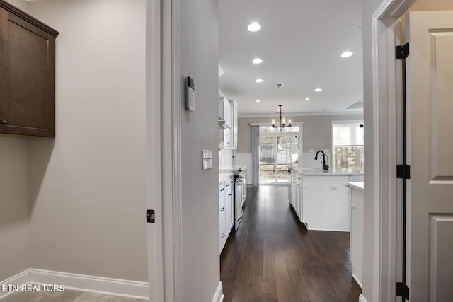 hallway with an inviting chandelier, recessed lighting, a sink, dark wood-type flooring, and crown molding