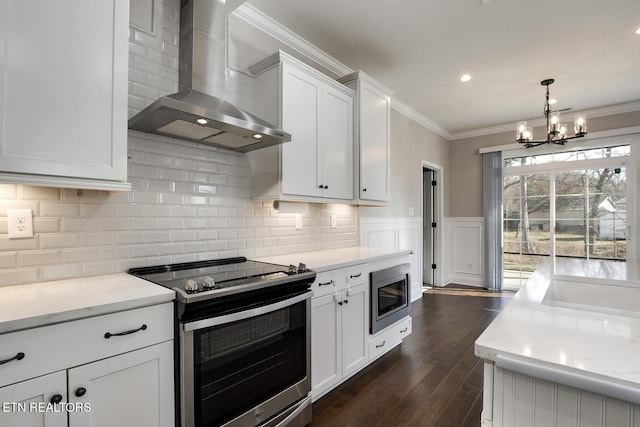 kitchen with crown molding, appliances with stainless steel finishes, dark wood-style floors, white cabinets, and wall chimney exhaust hood