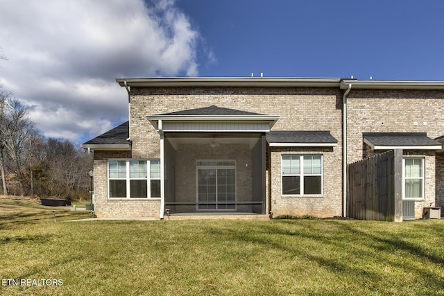 rear view of house featuring brick siding, a lawn, a ceiling fan, and a sunroom