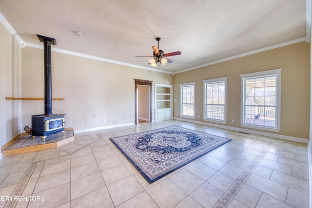 living room with a wood stove, ornamental molding, baseboards, and ceiling fan