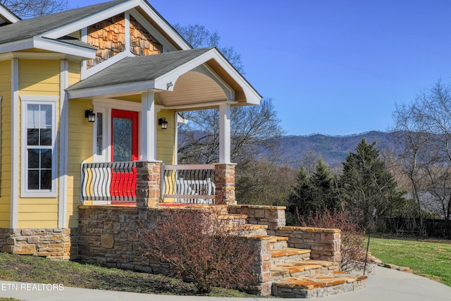 entrance to property featuring a mountain view, stone siding, a porch, and a shingled roof