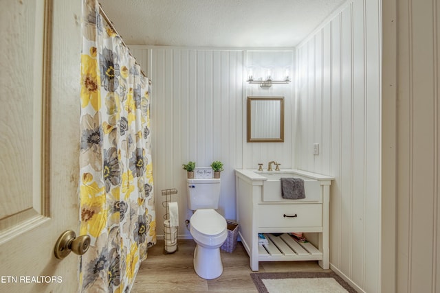 bathroom featuring curtained shower, toilet, vanity, wood finished floors, and a textured ceiling