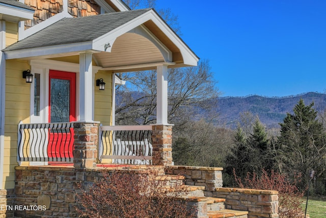 view of exterior entry featuring a mountain view, covered porch, and a shingled roof