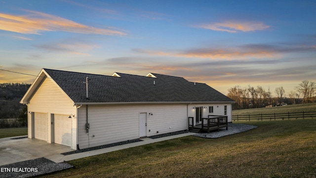 back of property with a detached garage, a lawn, fence, and roof with shingles