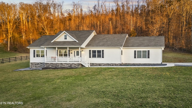 view of front of property featuring roof with shingles, covered porch, a front yard, and fence