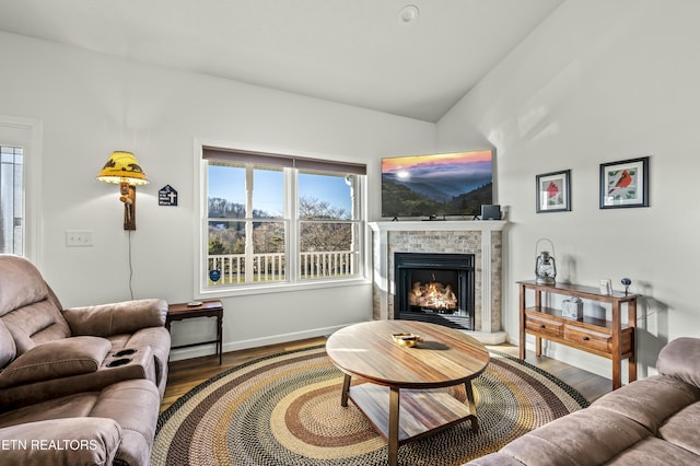 living room with baseboards, a warm lit fireplace, wood finished floors, and vaulted ceiling