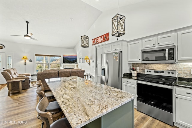 kitchen featuring a kitchen bar, light wood-style flooring, open floor plan, stainless steel appliances, and light stone countertops