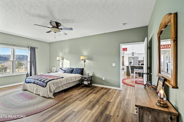 bedroom with baseboards, wood finished floors, stainless steel fridge, a textured ceiling, and a ceiling fan