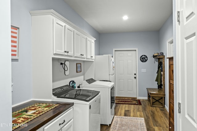 clothes washing area featuring dark wood finished floors, washing machine and dryer, cabinet space, and baseboards