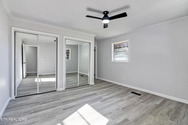 unfurnished bedroom featuring wood finished floors, baseboards, visible vents, multiple closets, and crown molding