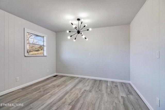 spare room featuring a notable chandelier, wood finished floors, and baseboards