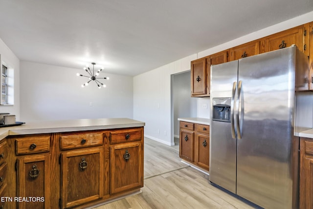 kitchen with stainless steel refrigerator with ice dispenser, an inviting chandelier, brown cabinetry, light wood finished floors, and light countertops