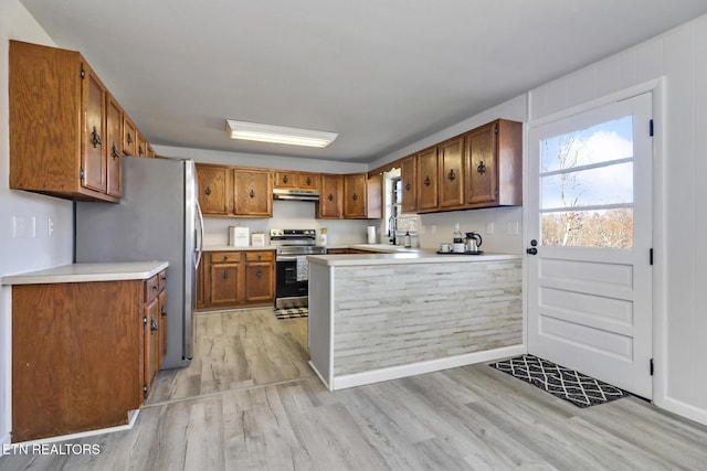 kitchen featuring under cabinet range hood, light wood-type flooring, brown cabinets, a peninsula, and stainless steel appliances