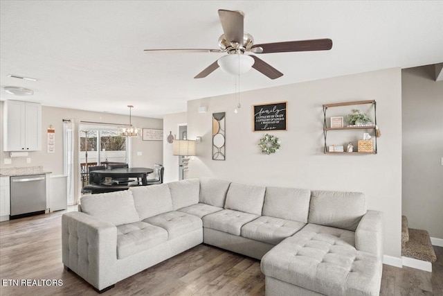 living room with light wood-style flooring, ceiling fan with notable chandelier, and baseboards