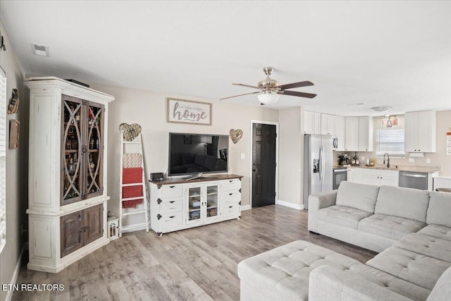 living room with light wood-type flooring, baseboards, visible vents, and ceiling fan