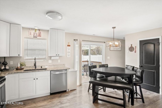 kitchen featuring stainless steel dishwasher, light stone counters, light wood finished floors, and a sink