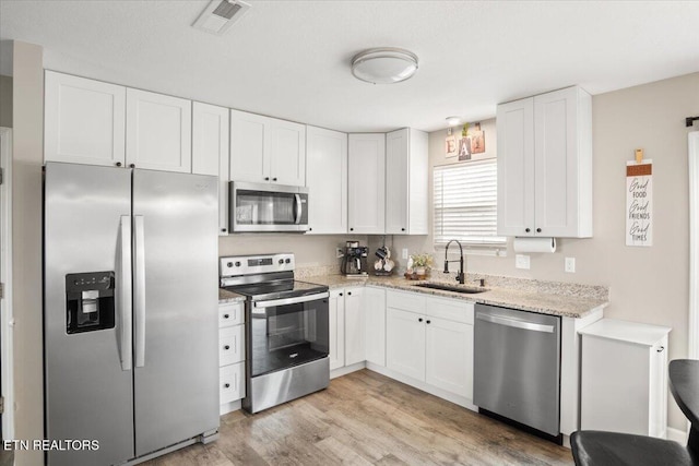 kitchen with light stone counters, light wood finished floors, a sink, white cabinets, and appliances with stainless steel finishes