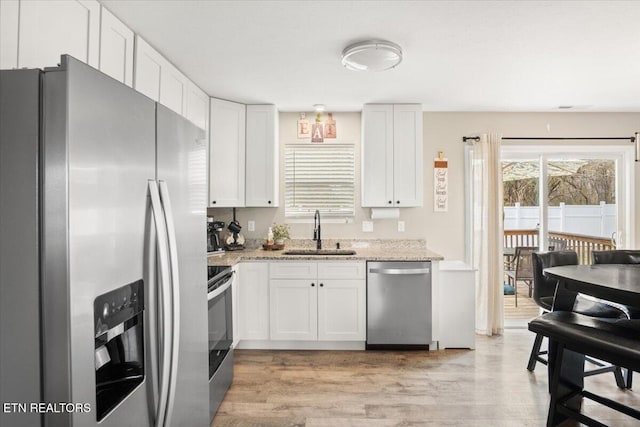 kitchen with light stone counters, a sink, stainless steel appliances, white cabinets, and light wood-style floors