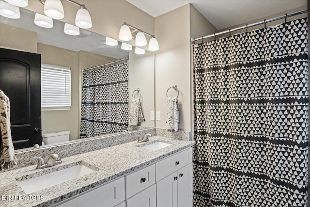 bathroom featuring a shower with shower curtain, double vanity, toilet, and a sink