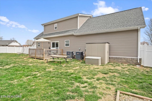 back of house featuring fence, a yard, a shingled roof, a wooden deck, and central AC unit