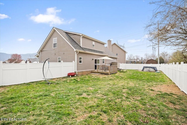 back of property with a fenced backyard, a lawn, and a wooden deck