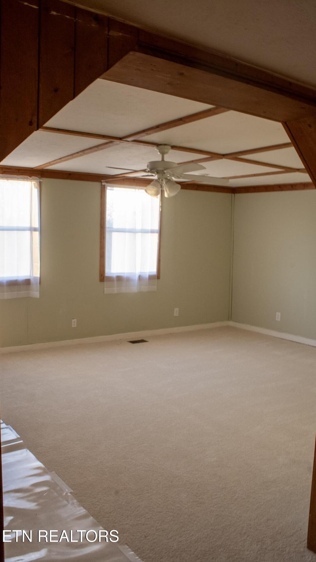 carpeted empty room with baseboards, plenty of natural light, beam ceiling, and a ceiling fan