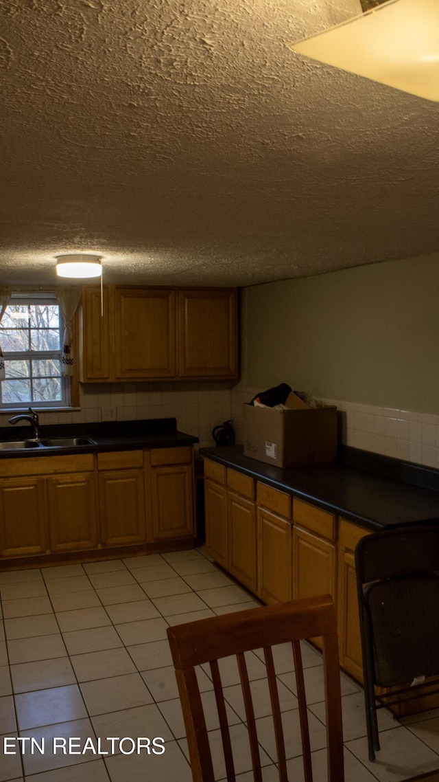 kitchen with dark countertops, brown cabinetry, light tile patterned flooring, a textured ceiling, and a sink