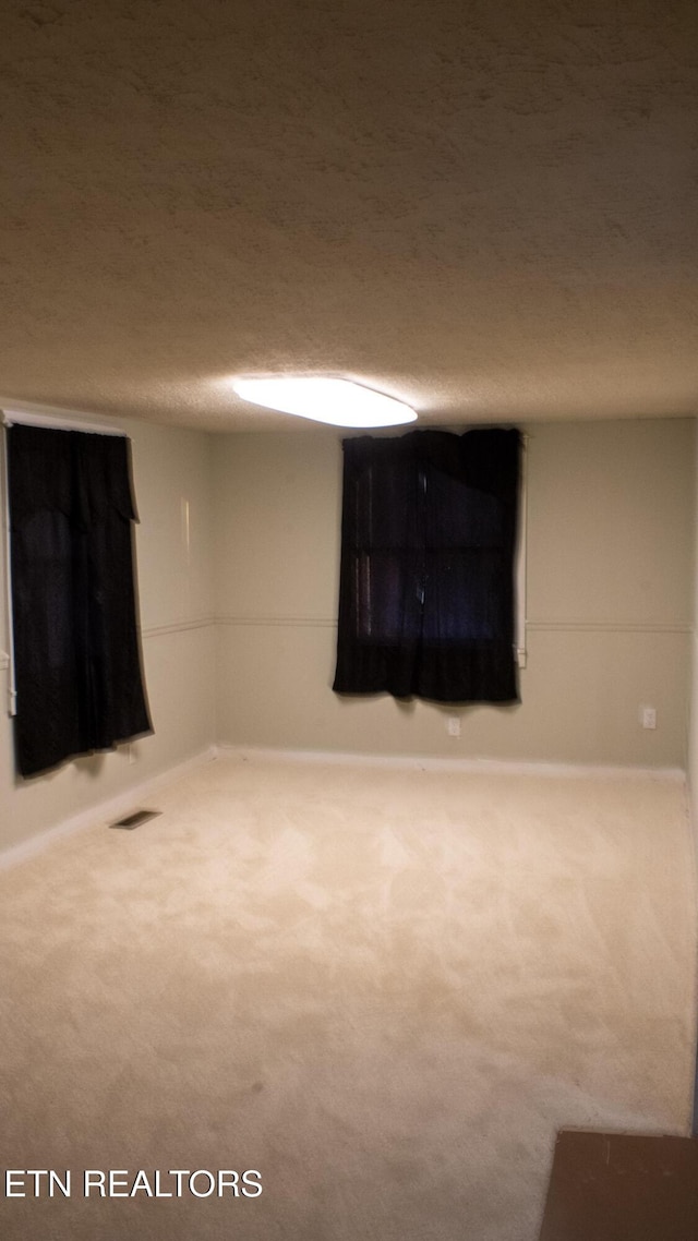 finished below grade area featuring baseboards, visible vents, a textured ceiling, and carpet