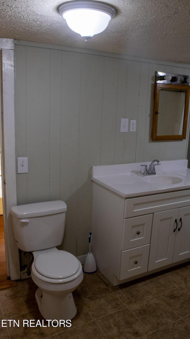 half bathroom featuring tile patterned floors, a textured ceiling, toilet, and vanity