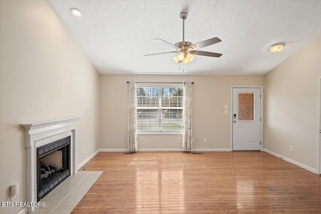 unfurnished living room featuring wood finished floors, a ceiling fan, baseboards, and a tile fireplace