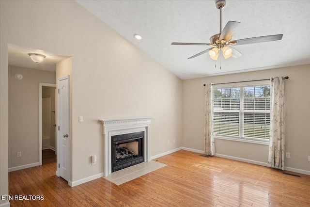 unfurnished living room with a fireplace with flush hearth, a ceiling fan, hardwood / wood-style flooring, a textured ceiling, and baseboards