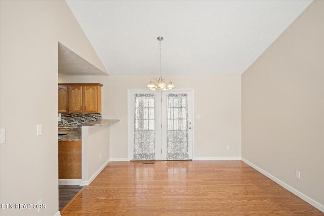 unfurnished dining area with a chandelier, light wood finished floors, baseboards, and vaulted ceiling