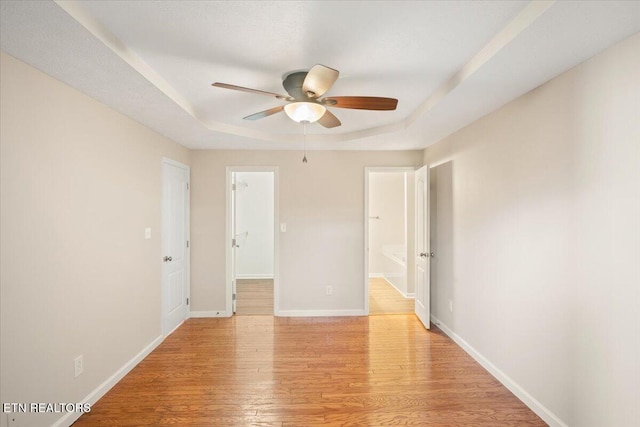 unfurnished room with light wood-style flooring, a raised ceiling, baseboards, and ceiling fan