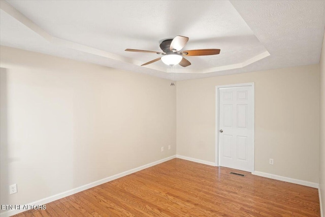 empty room with visible vents, a tray ceiling, wood finished floors, baseboards, and ceiling fan