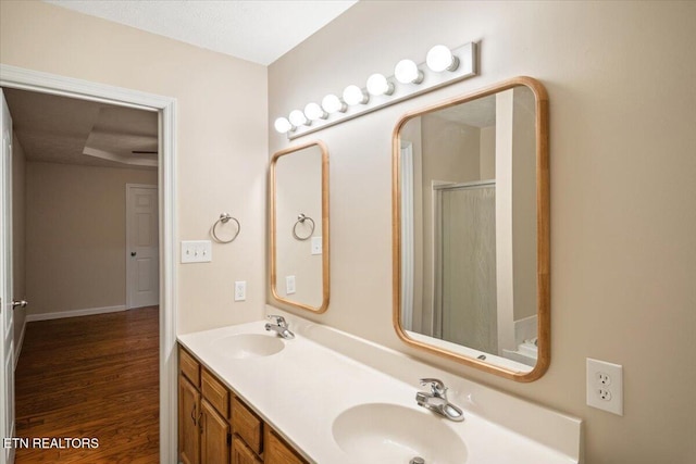 full bathroom featuring double vanity, a shower with shower door, wood finished floors, and a sink