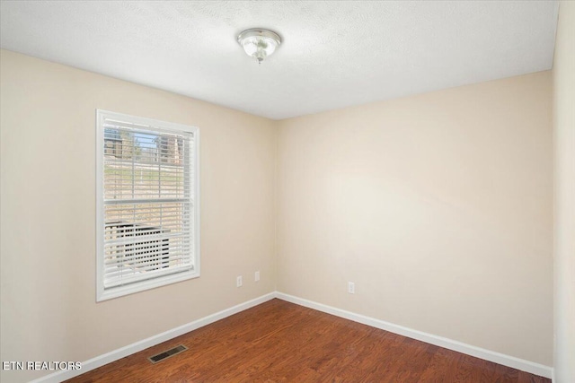 unfurnished room featuring visible vents, dark wood-style floors, and baseboards