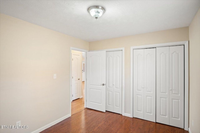 unfurnished bedroom featuring a textured ceiling, two closets, baseboards, and wood finished floors