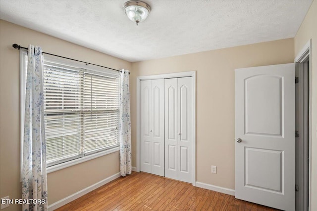 unfurnished bedroom featuring a closet, multiple windows, baseboards, and light wood-style flooring