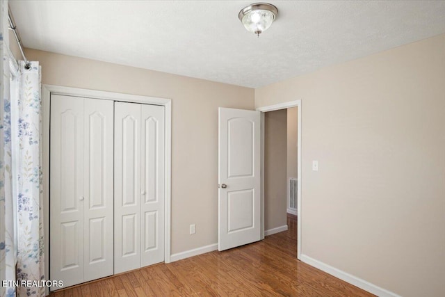 unfurnished bedroom with a closet, visible vents, baseboards, and wood finished floors