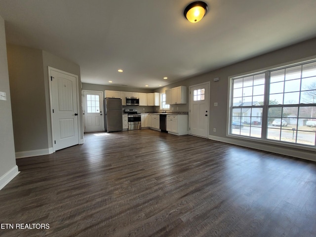 unfurnished living room with dark wood finished floors, plenty of natural light, and baseboards