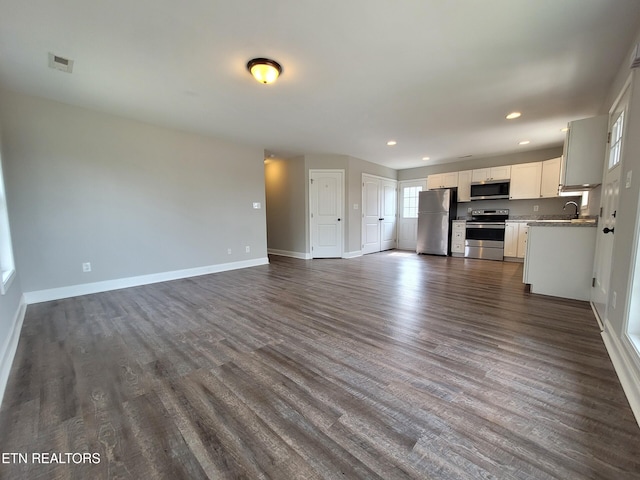 unfurnished living room featuring visible vents, baseboards, recessed lighting, dark wood-style floors, and a sink