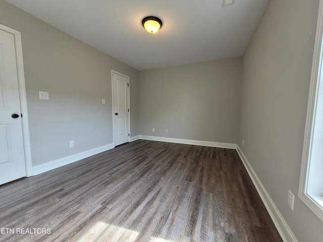 spare room with baseboards and dark wood-style flooring