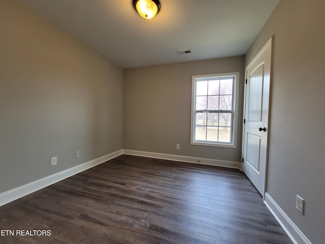 empty room featuring dark wood finished floors, visible vents, and baseboards