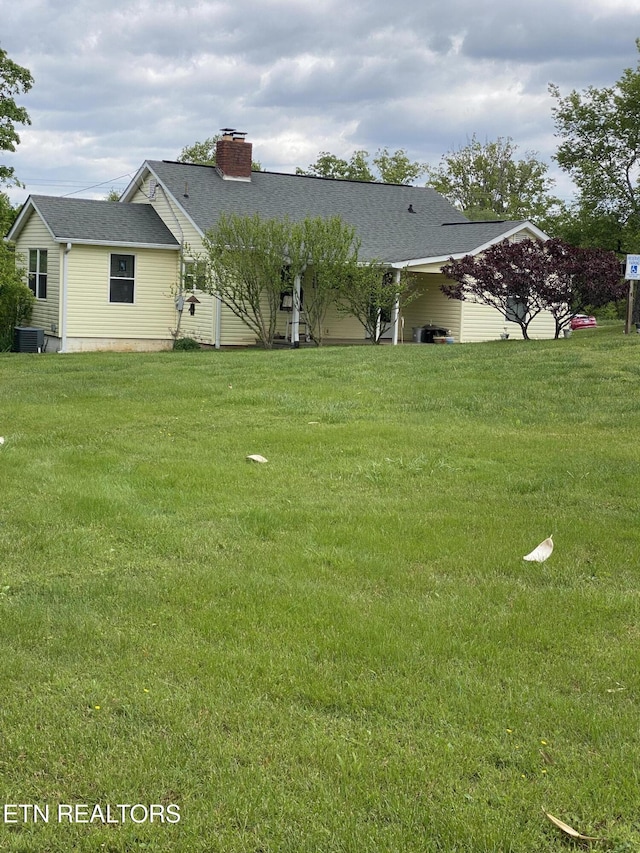 view of front of property featuring a chimney, a front lawn, and a shingled roof