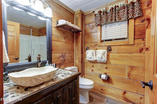 full bath featuring a shower with door, wood walls, toilet, and vanity