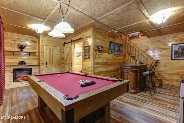 rec room featuring a barn door, a warm lit fireplace, wood finished floors, and wood walls